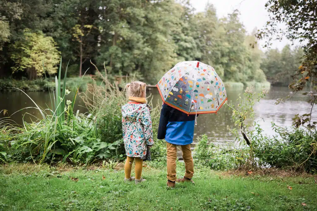 Deux enfants regardent un étang sous un parapluie