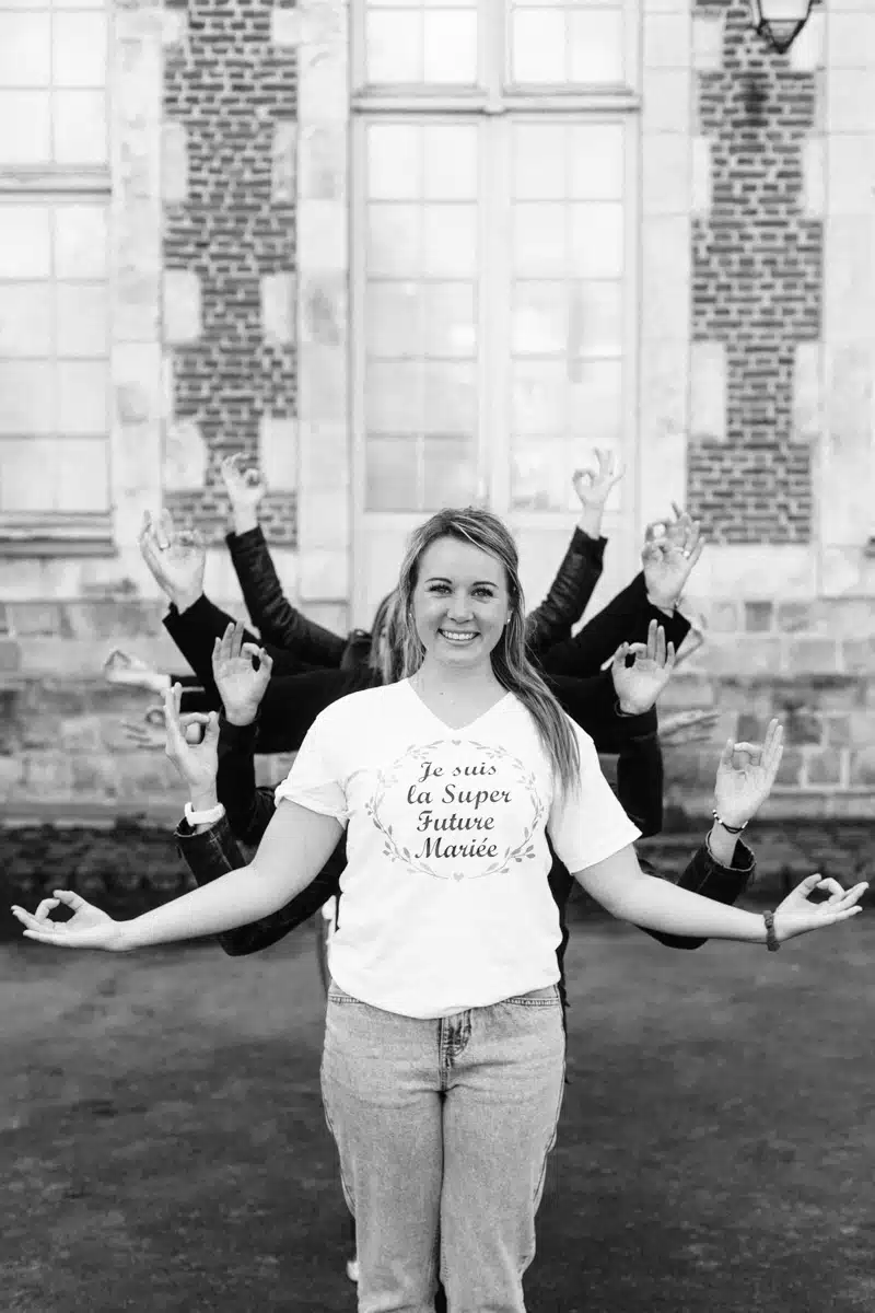 Future mariée en t-shirt personnalisé, les bras de ses amies derrière elle, photo EVJF en noir et blanc