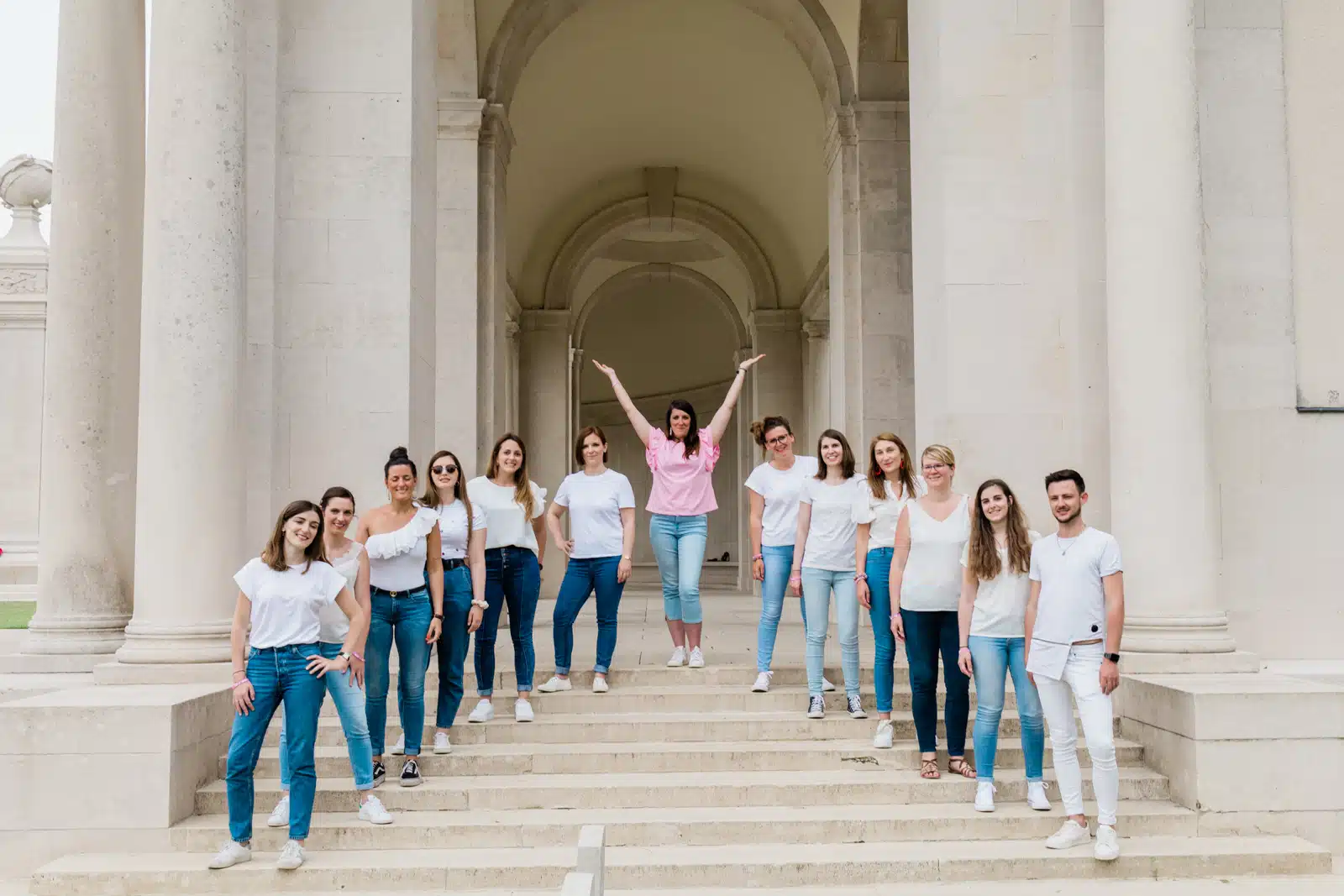Groupe d'amies sur les marches d'un bâtiment à colonnes, la future mariée bras levés, séance photo EVJF