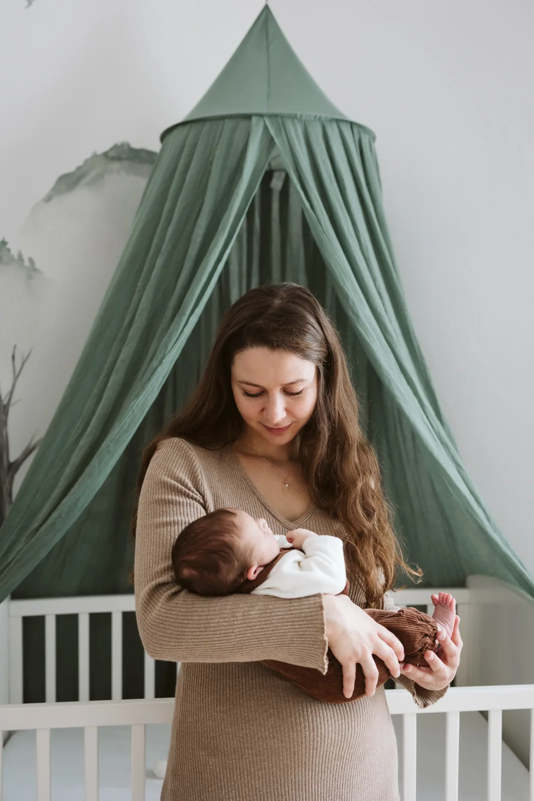 Maman portant son bebe devant le lit et le ciel de lit de sa chambre
