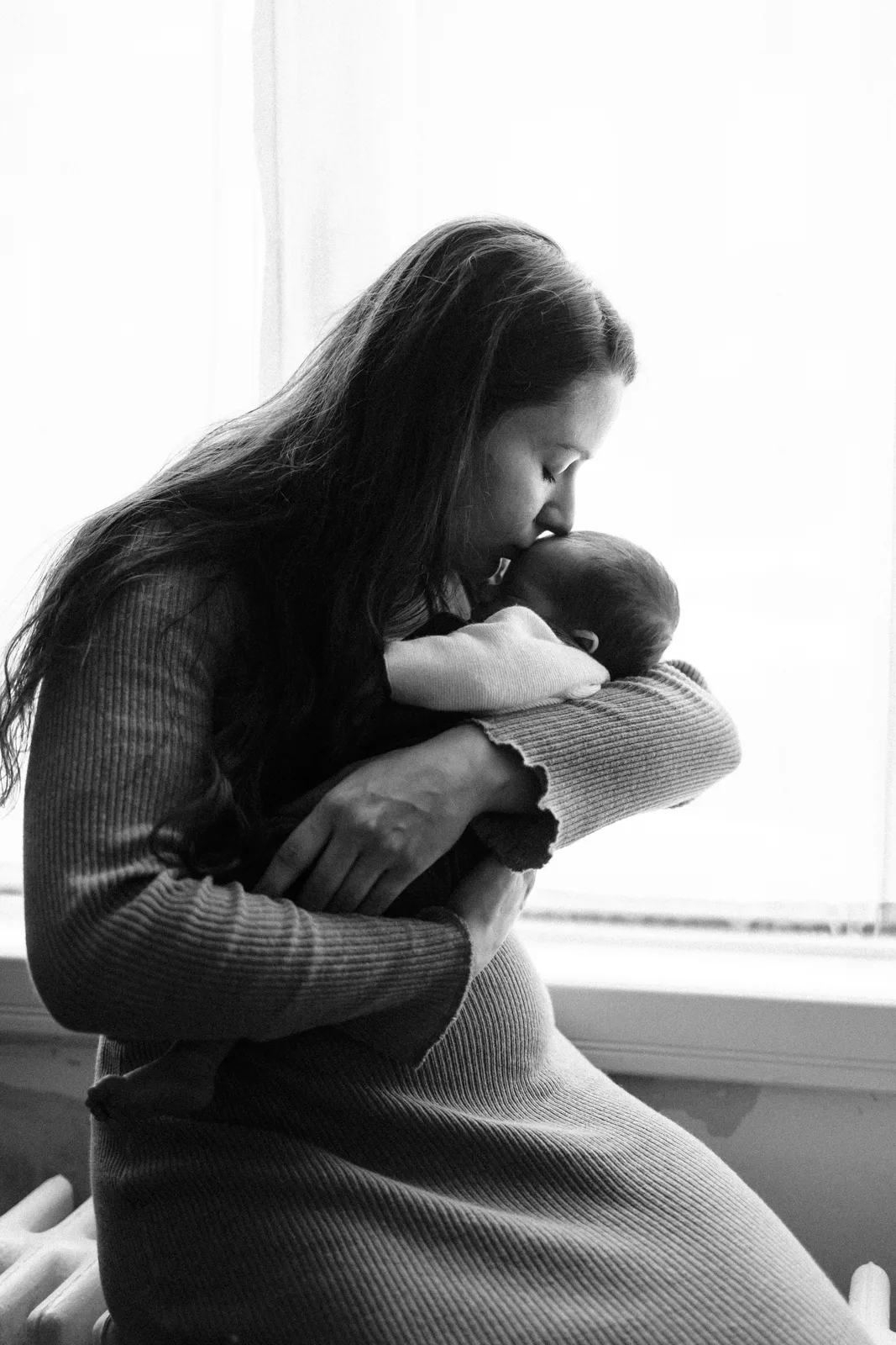 Maman calinant son nouveau-ne pres de la fenetre en noir et blanc