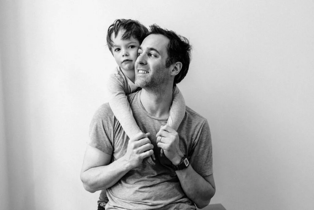 Père souriant portant son fils en noir et blanc.