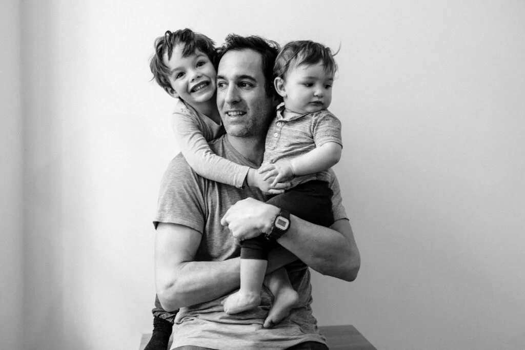 Père souriant avec deux enfants dans les bras.