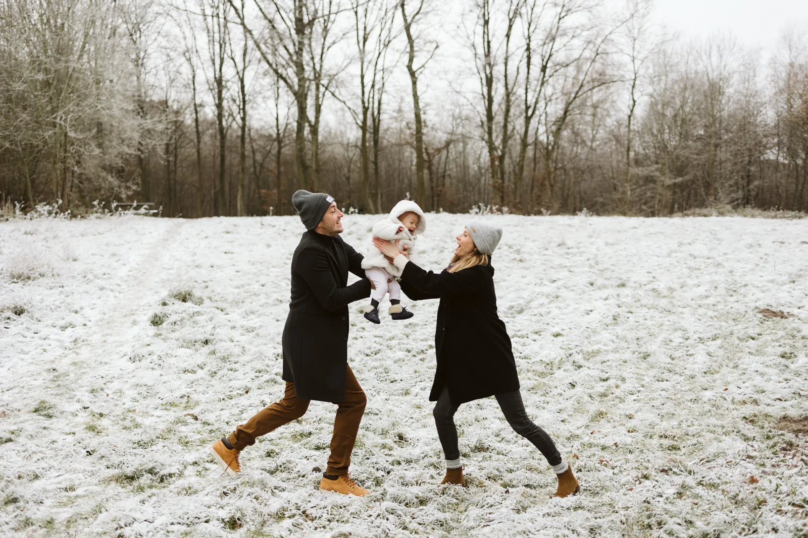 Parents jouant avec leur bebe dans la neige pendant une seance photo famille en hiver
