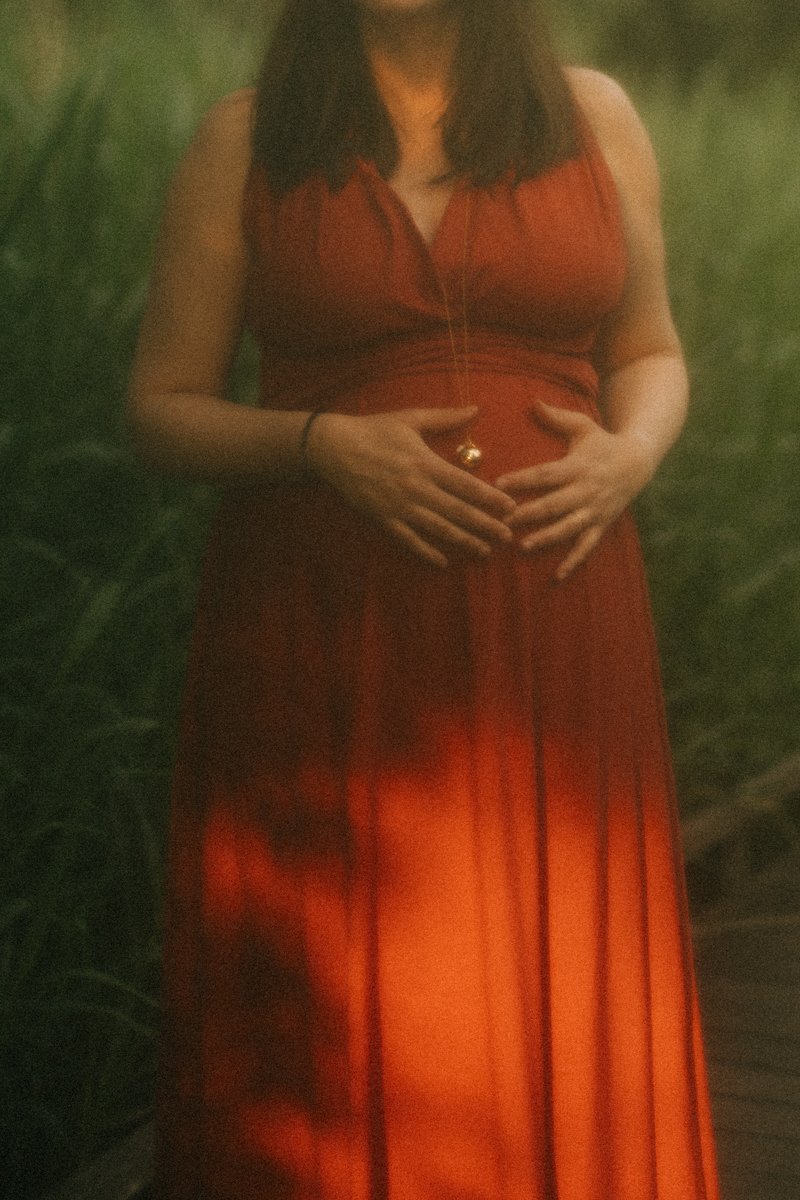 Gros plan sur les mains d’une future maman posées sur son ventre, robe rouge et bola de grossesse