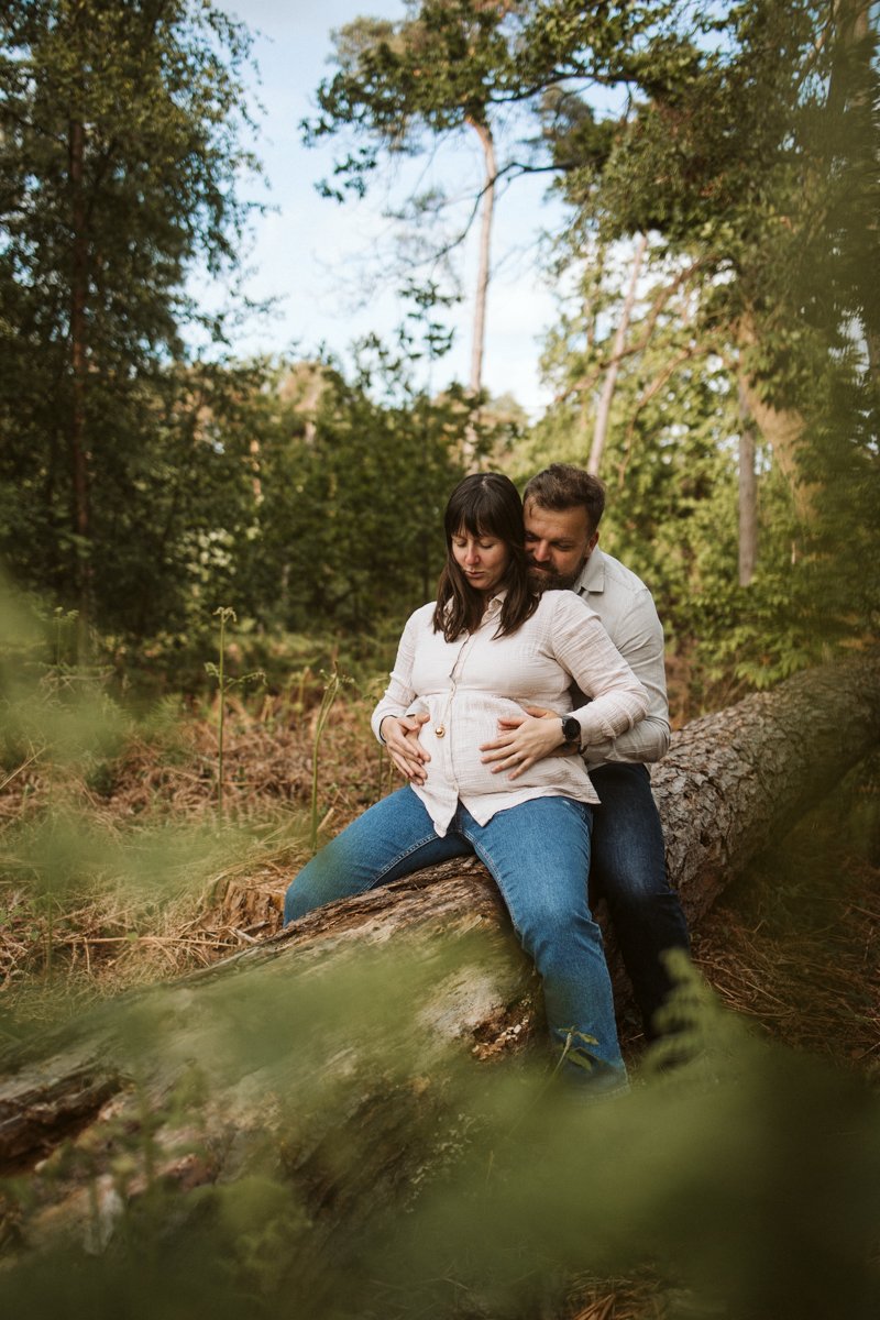 Futurs parents assis sur un tronc d’arbre en forêt, les mains du papa sur le ventre