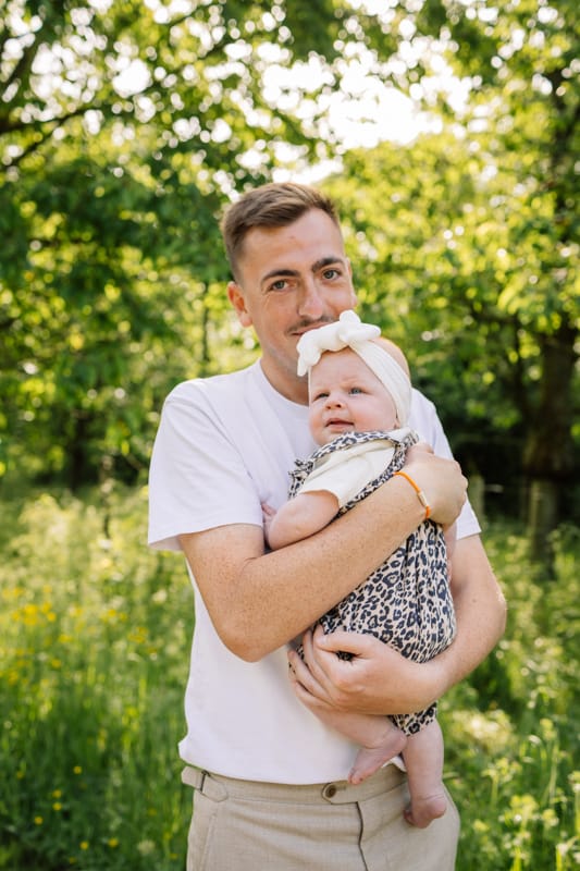 Papa tenant sa fille dans les bras pendant une seance photo famille en exterieur