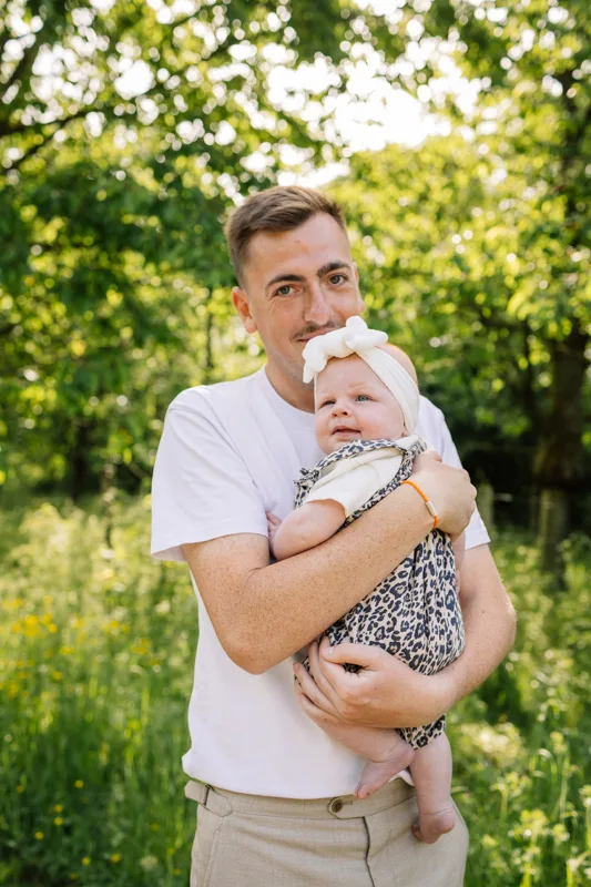 Papa tenant sa fille dans les bras pendant une seance photo famille en exterieur