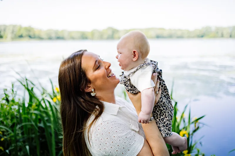 Maman soulevant son bebe en souriant au bord du lac du Heron